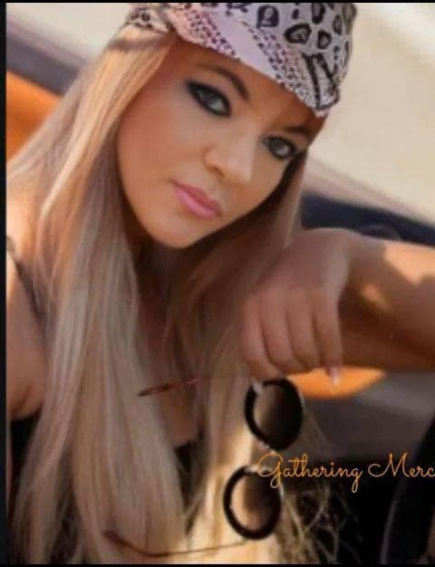 Blonde woman wearing a leopard print bandana and dark eye makeup, holding round sunglasses.